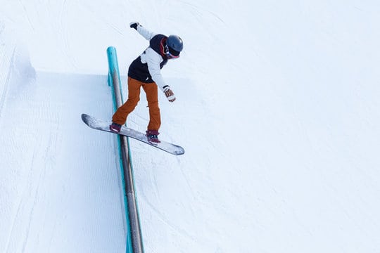 A brave man performs a rail slide on snowboard
