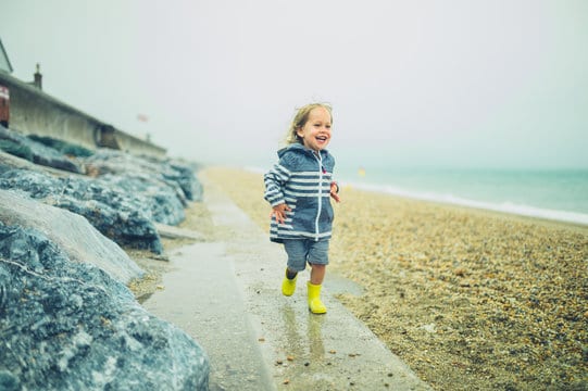 Little toddler running and playing on a rocky beach in the rain