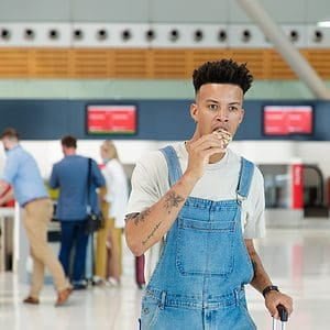 A Man in a Denim Overall Eating a Cookie at an Airport