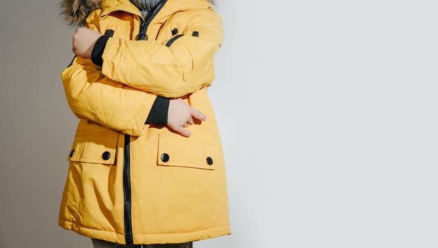 Front view of Child dressed in a yellow winter jacket with fur on the hood. The concept of dressing 