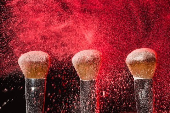 Make up, beauty, mineral cosmetic concept - powder brush on black background with red powder splashe