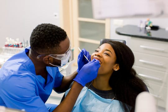 Male african dentist examining a patient with tools in dental clinic.