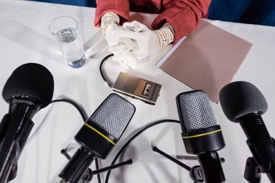 partial view of woman in white gloves, microphones and vintage dictaphone on white table