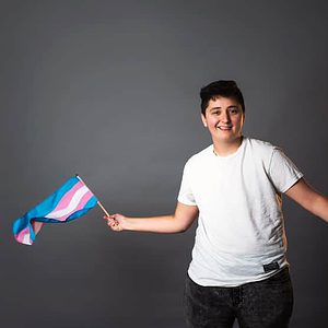 smiling person waving trans pride flag